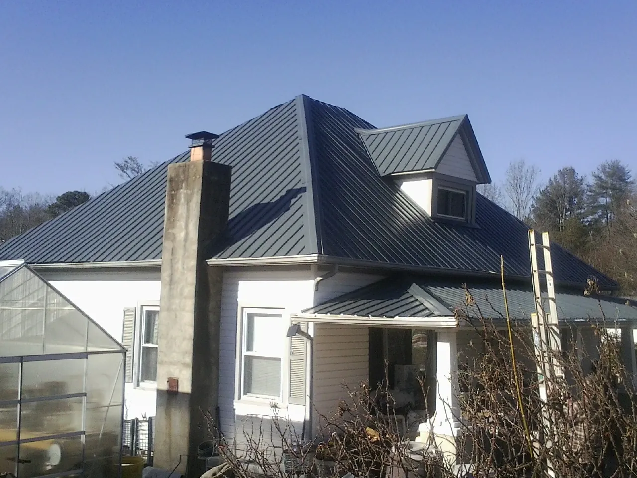 Dark blue standing seam metal roof on a white farmhouse with dormer — Slate & Tile Roof Repair by Roofing Brothers in Moorland