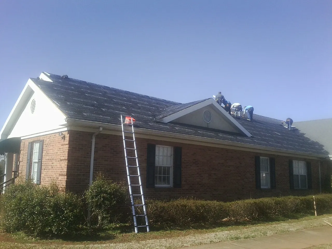 Crew tearing shingles off a brick ranch roof with a ladder set — Metal Roof Repair work by our crew in Moorland