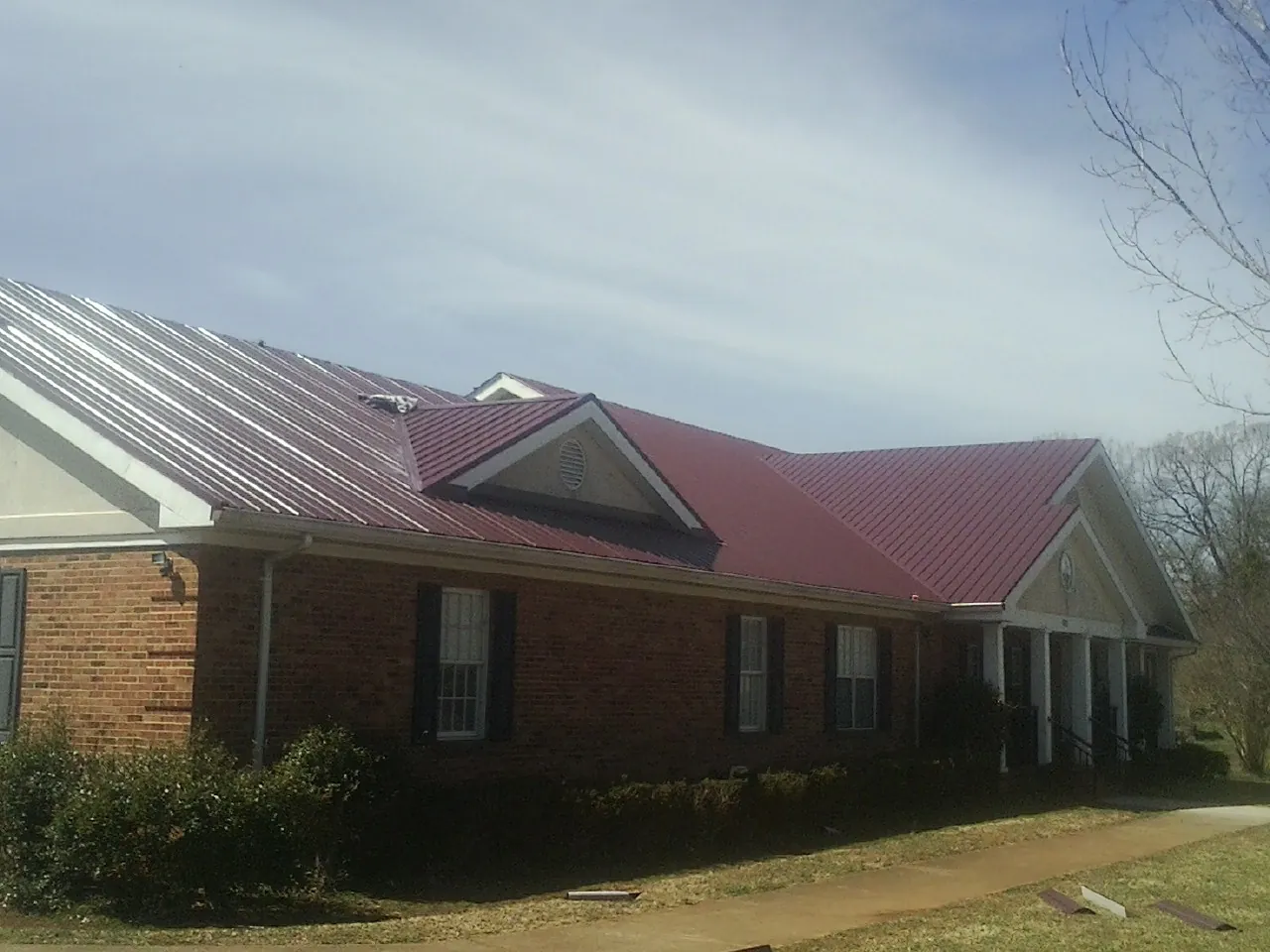 Red metal roof with gabled entries on a long brick building, from a Hail Damage Roof Repair job in Moorland