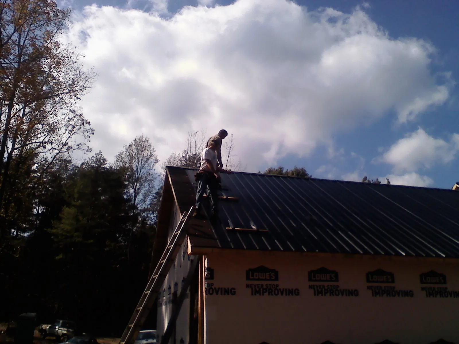 Roofer fastening dark metal panels high against a cloudy sky, from a Roof Inspection job in Moorland