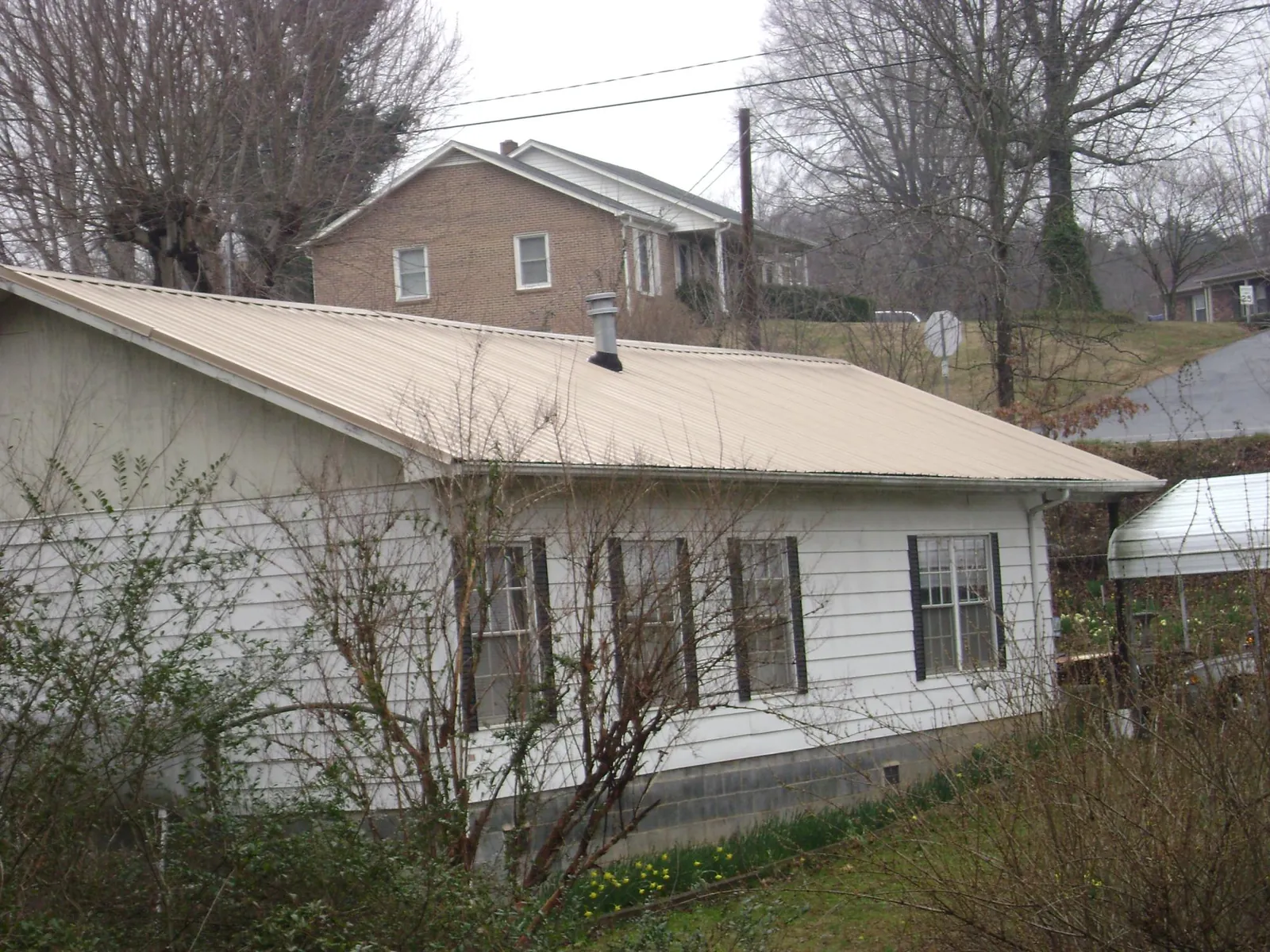 Tan metal roof on a white sided house set into a hillside — Commercial Roofing by Roofing Brothers in Moorland