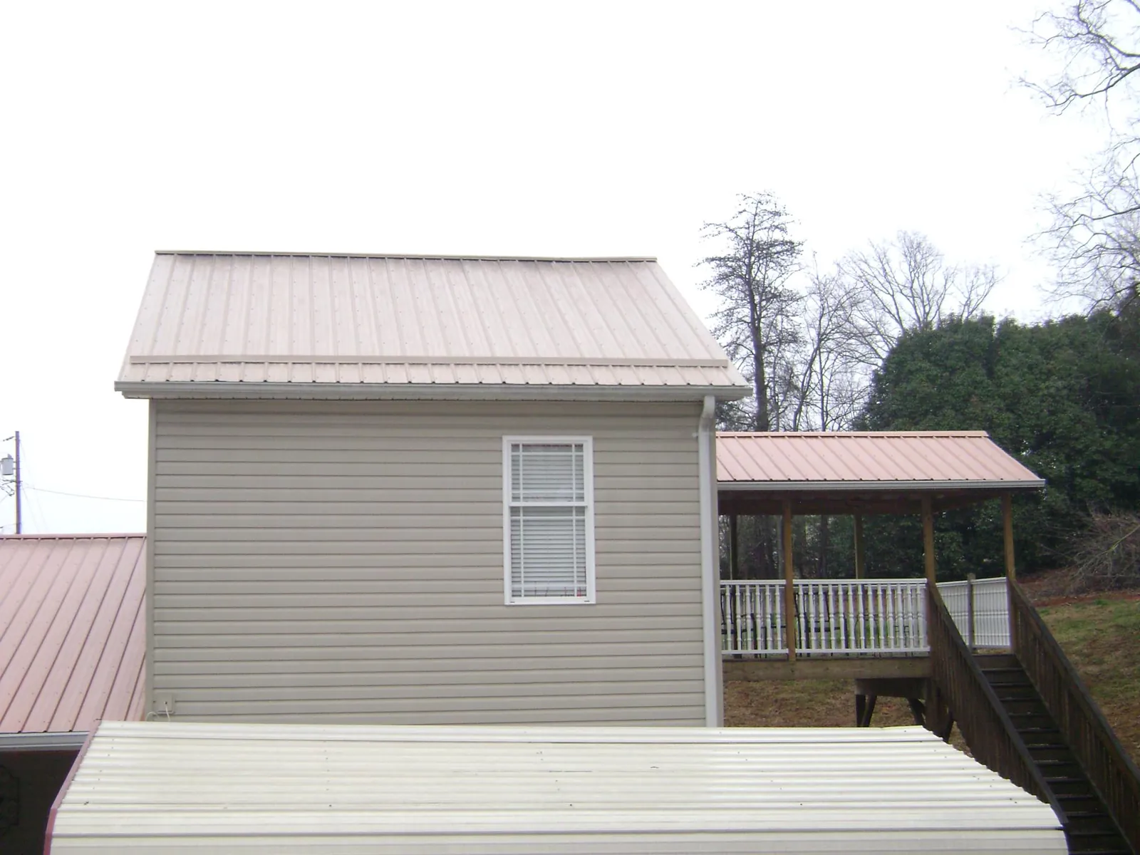 Tan metal roofs on a two story addition and attached porch, from a Roof Replacement job in Moorland